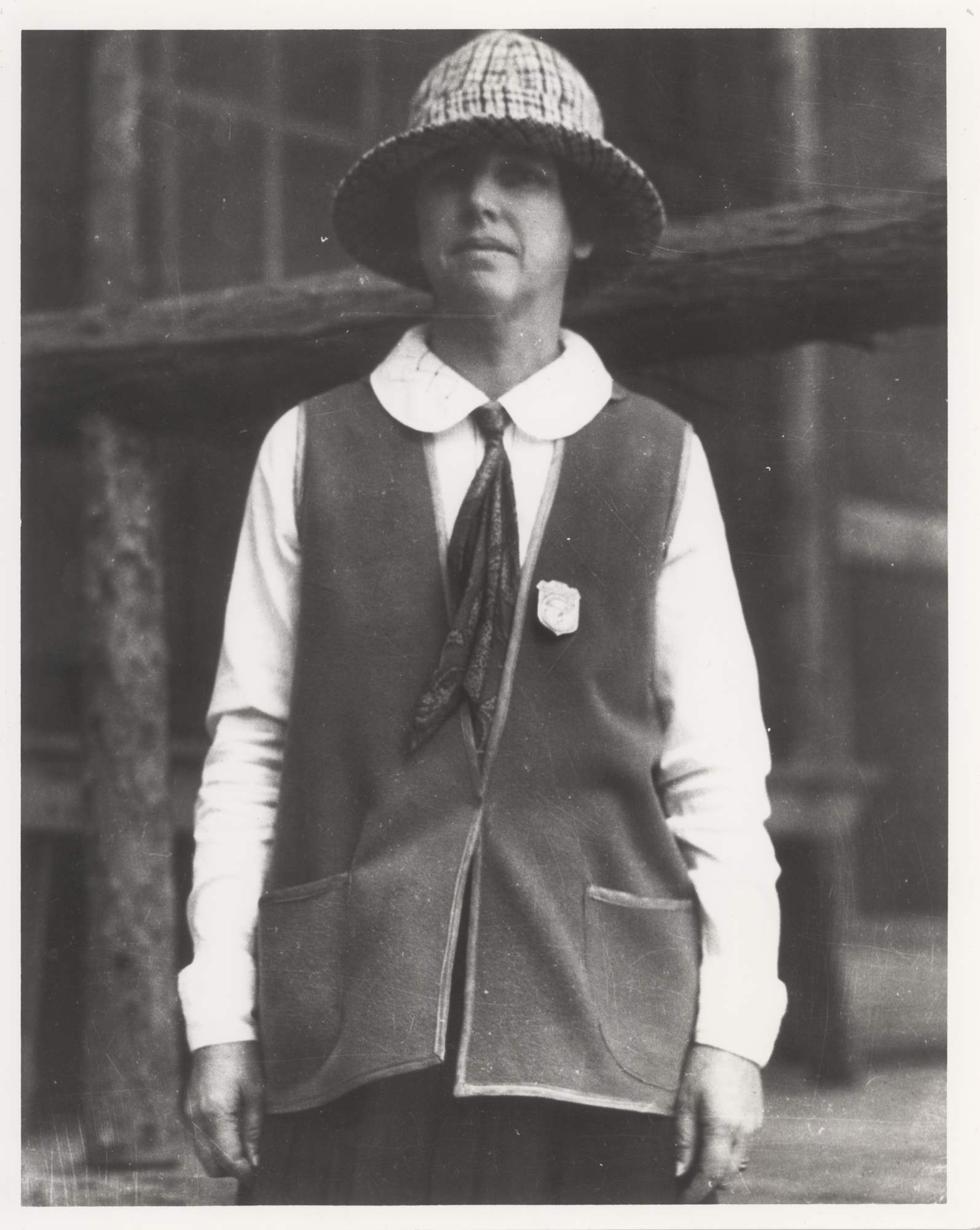 Martha Bingaman poses wearing a skirt, blouse, scarf, soft brimmed hat, and vest. She has a shield-shaped badge pinned to the vest.